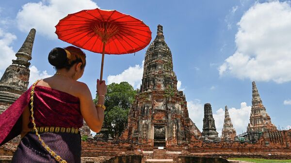 In this photo taken on June 27, 2021, a visitor wearing a traditional costume and holding an umbrella arrives at the 17th century Wat Chaiwatthanaram temple complex in the ancient capital of Ayutthaya, north of Bangkok. - Sputnik International