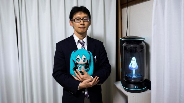 In this photograph taken on November 10, 2018 Japanese Akihiko Kondo poses next to a hologram of Japanese virtual reality singer Hatsune Miku as he holds the doll version of her at his apartment in Tokyo, a week after marrying her. - Akihiko Kondo, who is an administrator at a school, married to a Japanese virtual reality singer called Hatsune Miku in early November 2018 - Sputnik International