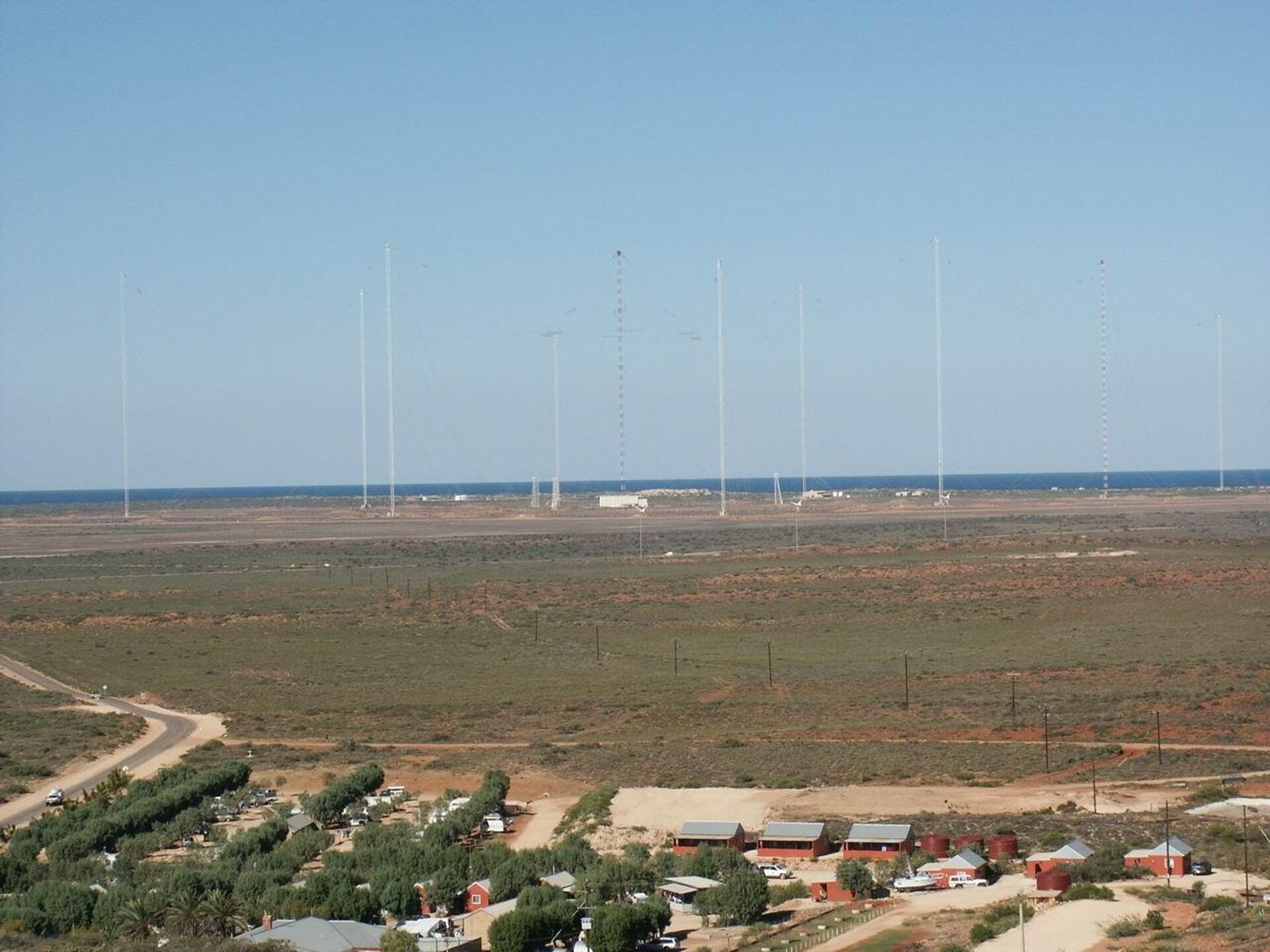 Naval Communication Station Harold E. Holt near Exmouth, Western Australia. The radio masts are part of a large wire antenna which is used to transmit very low frequency (VLF) radio waves to communicate with submerged submarines. This type of antenna is known as a Goliath, a type of umbrella antenna, but has been heavily modified. It consists of a ring of steel masts which support a network of horizontal cables radiating from the central mast. The central mast acts as the radiating element, while the horizontal cables serve as a capacitive top-load, creating a large capacitor with the ground. This serves to increase the current in the central radiator, increasing the radiated power. - Sputnik International, 1920, 16.05.2022