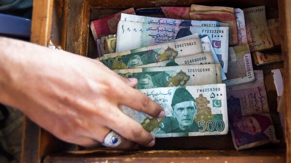 A Pakistani man counts Pakistan's rupees at his shop in Karachi on May 16, 2019 - Sputnik International