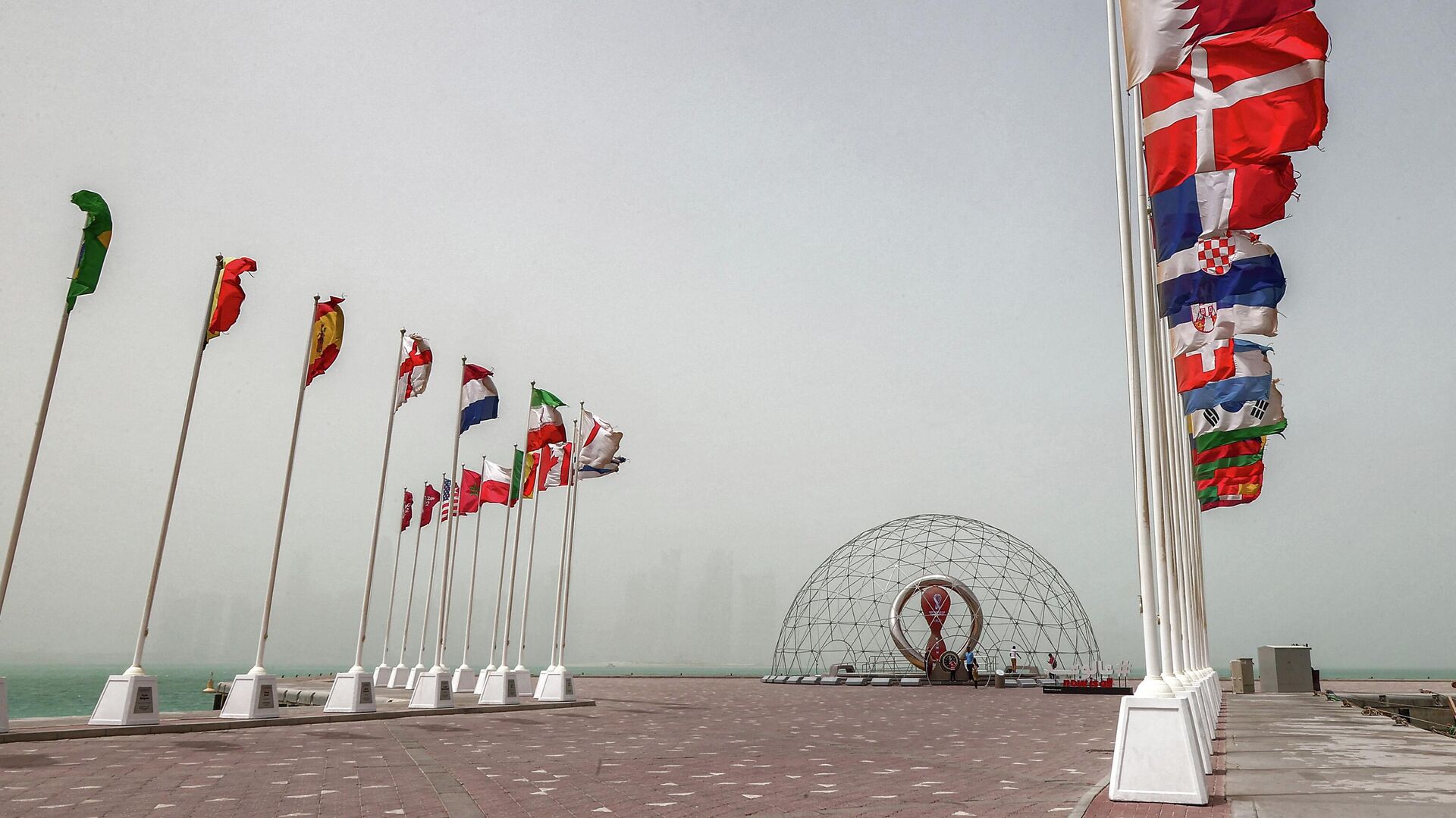 The flags of nations taking part in the Qatar 2022 FIFA World Cup fly Qatar's capital Doha during a heavy dust storm on May 17, 2022 as the skyline behind is obscured in the haze. - Sputnik International, 1920, 28.05.2022