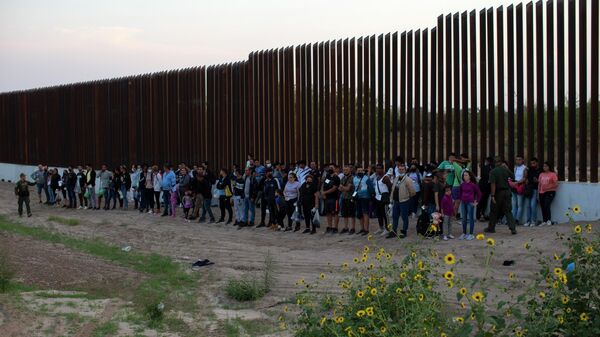 A group of migrants stand next to the border wall as they wait to get taken away by the Border Patrol in Eagle Pass, Texas, Saturday, May 21, 2022 - Sputnik International