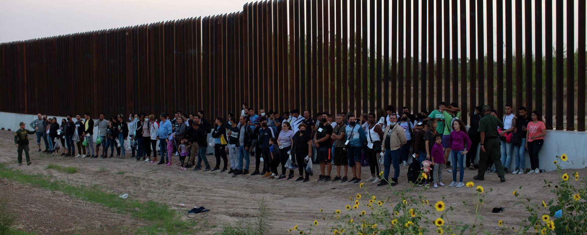 A group of migrants stand next to the border wall as they wait to get taken away by the Border Patrol in Eagle Pass, Texas, Saturday, May 21, 2022 - Sputnik International, 1920, 15.11.2022