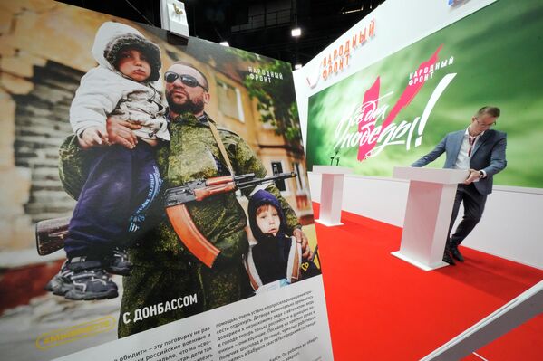 A man sets a tribune at a stand of the Russian People&#x27;s Front movement with a poster showing a Donbass serviceman with two children, at the St. Petersburg International Economic Forum in St. Petersburg. - Sputnik International
