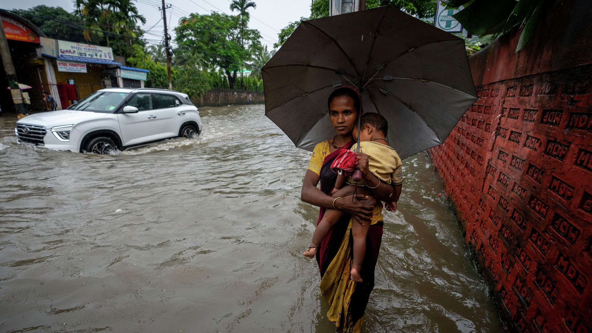 A woman carries a child and wades through a flooded street during heavy rainfall in Gauhati, India, Thursday, June 16, 2022 - Sputnik International, 1920, 20.06.2022