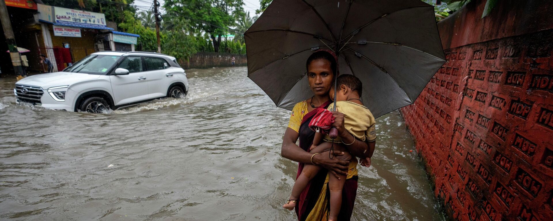 A woman carries a child and wades through a flooded street during heavy rainfall in Gauhati, India, Thursday, June 16, 2022 - Sputnik International, 1920, 20.06.2022