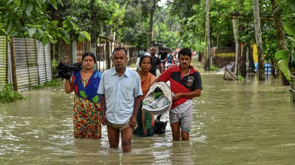 People wade through flood waters in Solmara of Nalbari district, in India's Assam state on June 19, 2022 - Sputnik International