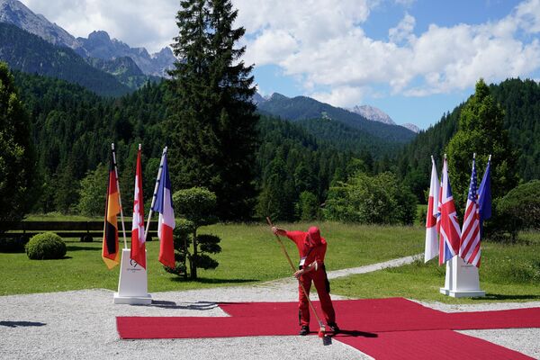 A worker cleans the red carpet on 26 June 2022 to welcome world leaders against the background of the Bavarian mountains at Elmau Castle, southern Germany, where the German Chancellor hosts a summit of the Group of Seven rich nations (G7). - Sputnik International