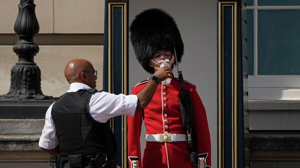 A police officer givers water to a British soldier wearing a traditional bearskin hat, on guard duty outside Buckingham Palace, during hot weather in London, Monday, July 18, 2022. - Sputnik International