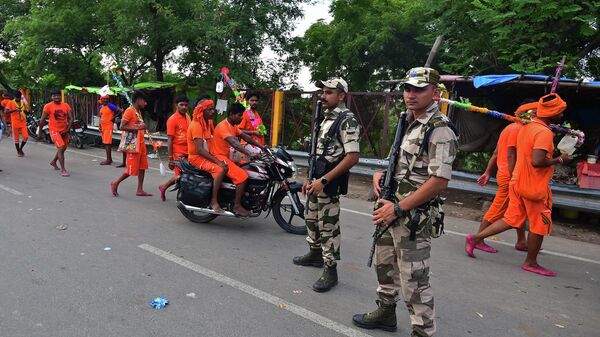 Members of security personnel stand guard as Kanwariyas, devotees of the Hindu deity Shiva, take part in their ritualistic walk in Allahabad on July 24, 2022 - Sputnik International