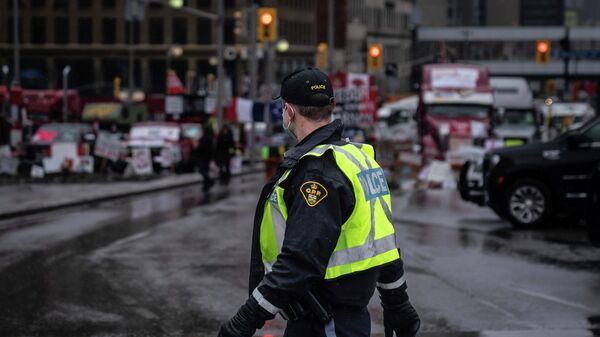 An Ontario Provincial Police officer walks in front of a row of trucks parked on the street near the Canadian parliament building in Ottawa on Thursday, Feb. 17, 2022. Hundreds of truckers clogging the streets of Canada's capital city in a protest against COVID-19 restrictions are bracing for a possible police crackdown. (AP Photo/Robert Bumsted) - Sputnik International