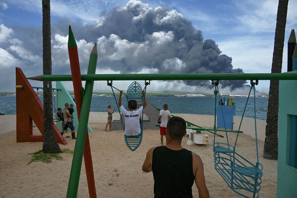 Black smoke from the massive fire at a fuel depot is seen while children play at a park in Matanzas, Cuba, on August 8, 2022. - Sputnik International