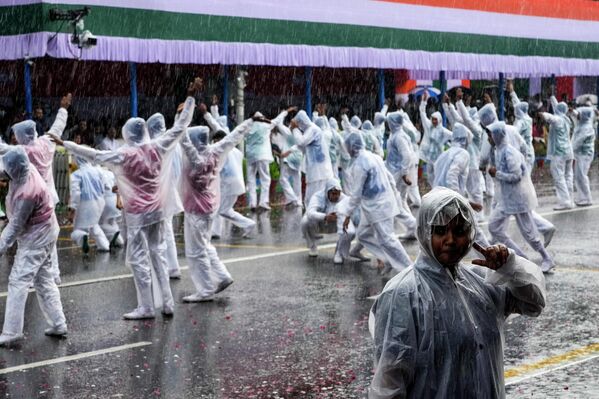 A policewoman tries to listen to an earphone as school students take part in a cultural event wearing raincoats as it rains during Independence Day celebrations in Kolkata, India, Monday, Aug. 15, 2022. - Sputnik International
