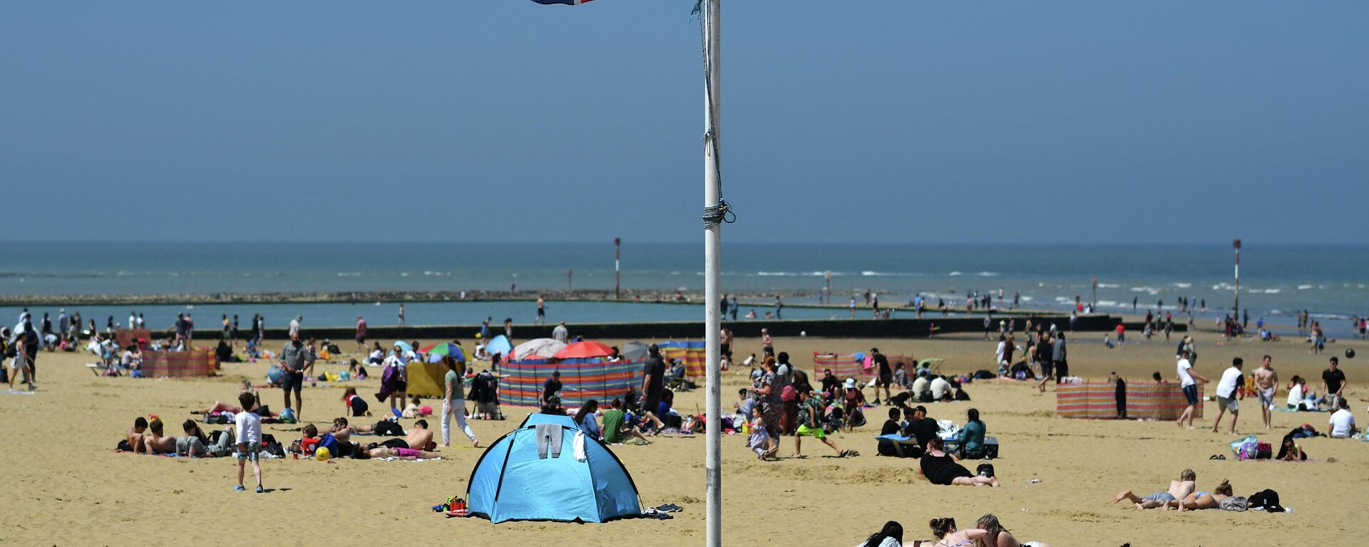 A Union flag flutters in the breeze as sunbathers take advantage of the fine weather on the beach on the coast at Margate, east of London on May 31, 2021, as fine and dry conditions continue in the UK on what could be the hottest day of the year so far - Sputnik International, 1920, 19.08.2022