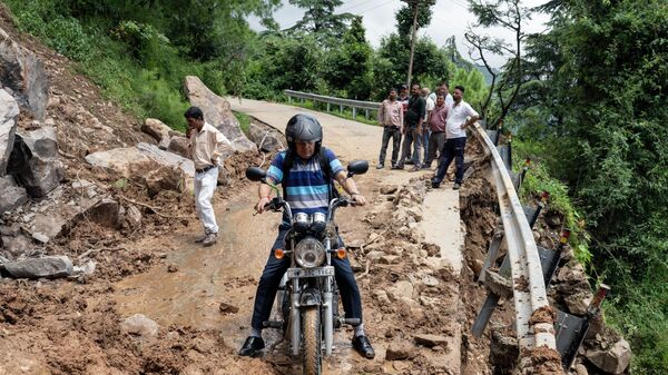 A motorcyclist tries to drive past mud and debris after a landslide blocked a road in Dharmsala, Himachal Pradesh state, India, Sunday, Aug. 21, 2022. - Sputnik International