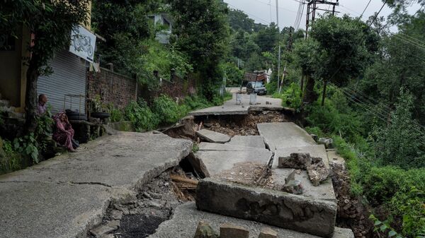 A man and woman sit next to a road, a part of which has caved in due to heavy rain in Dharmsala, Himachal Pradesh state, India, Sunday, Aug. 21, 2022.  - Sputnik International