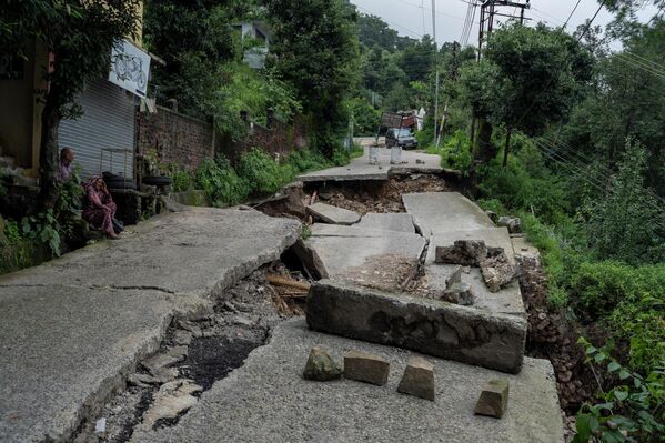 A man and woman sit next to a road, part of which has caved in because of heavy rains in Dharmshala, Himachal Pradesh state, India, Sunday, 21 August 2022. - Sputnik International