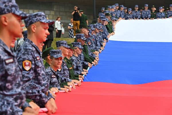 Russian soldiers and National Guard officers hold a huge tricolor near the Victory Museum in Moscow, August 22, 2022. - Sputnik International