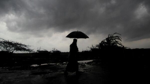 FILE - A villager holds an umbrella as dark clouds loom over Balasore district in Odisha, India - Sputnik International