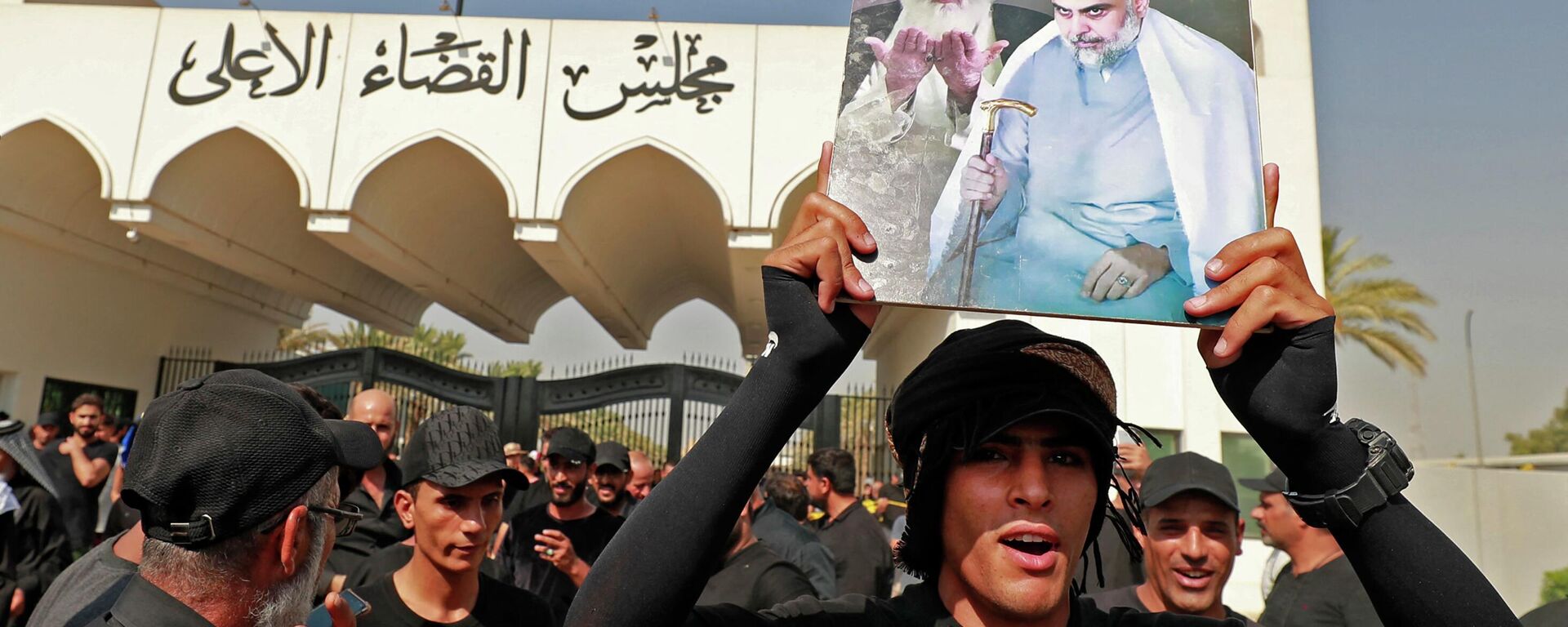A man lifts a placard depicting Iraqi Shiite cleric Muqtada al-Sadr (R) and upporters of Iraqi Shiite cleric Muqtada al-Sadr his late father Grand Ayatollah Mohammed Sadeq al-Sadr, as his supporters gather outside the headquarters of the Supreme Judicial Council, Iraq's highest judicial body, in the capital Baghdad, on August 23, 2022.  - Sputnik International, 1920, 23.08.2022