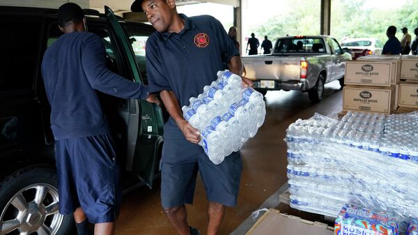 A Jackson, Miss., Fire Department firefighter puts cases of bottled water in a resident's SUV, Aug. 18, 2022, as part of the city's response to longstanding water system problems.  - Sputnik International