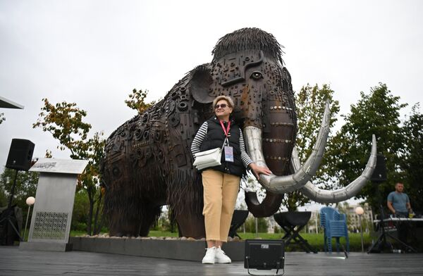 A participant of the Eastern Economic Forum in Vladivostok taking pictures with a mammoth sculpture. - Sputnik International