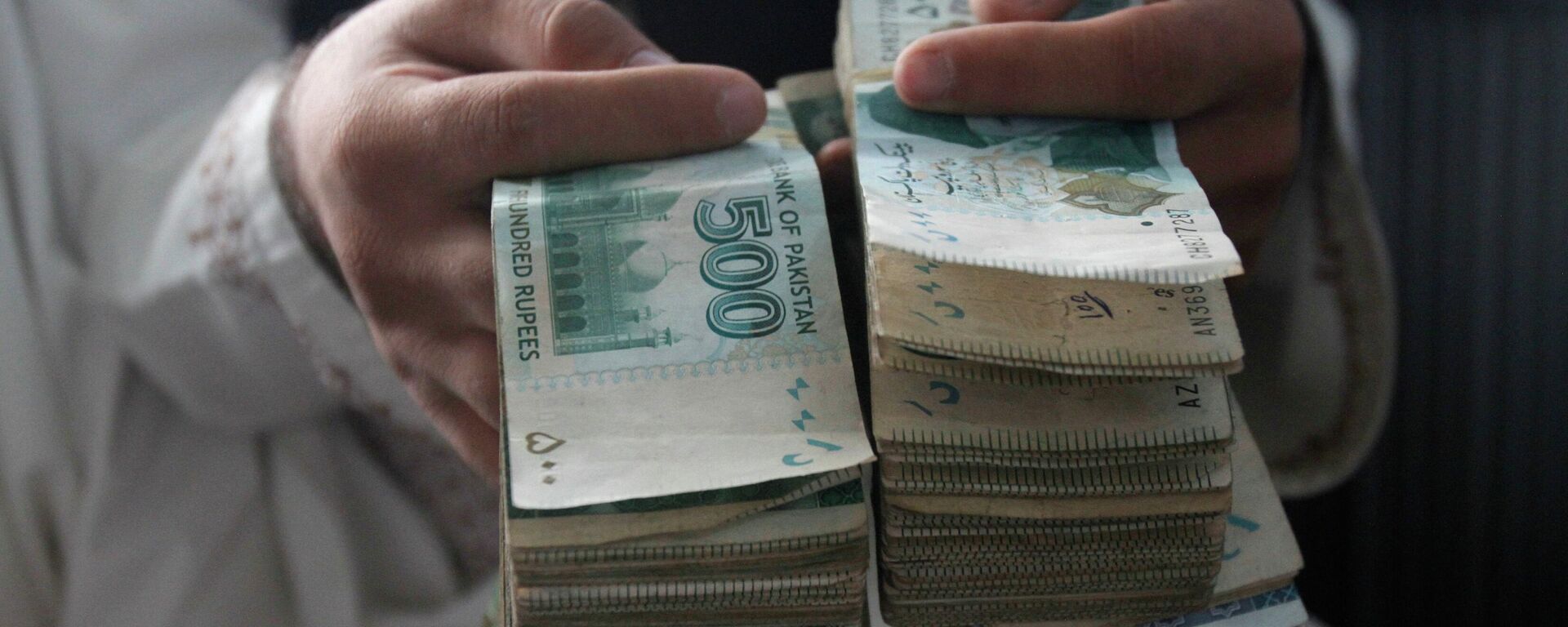 An Afghan money changer holds Pakistani currency bundles at the money exchange market in Kandahar south of Kabul, Afghanistan, Sunday, Aug. 7, 2016. - Sputnik International, 1920, 20.09.2022