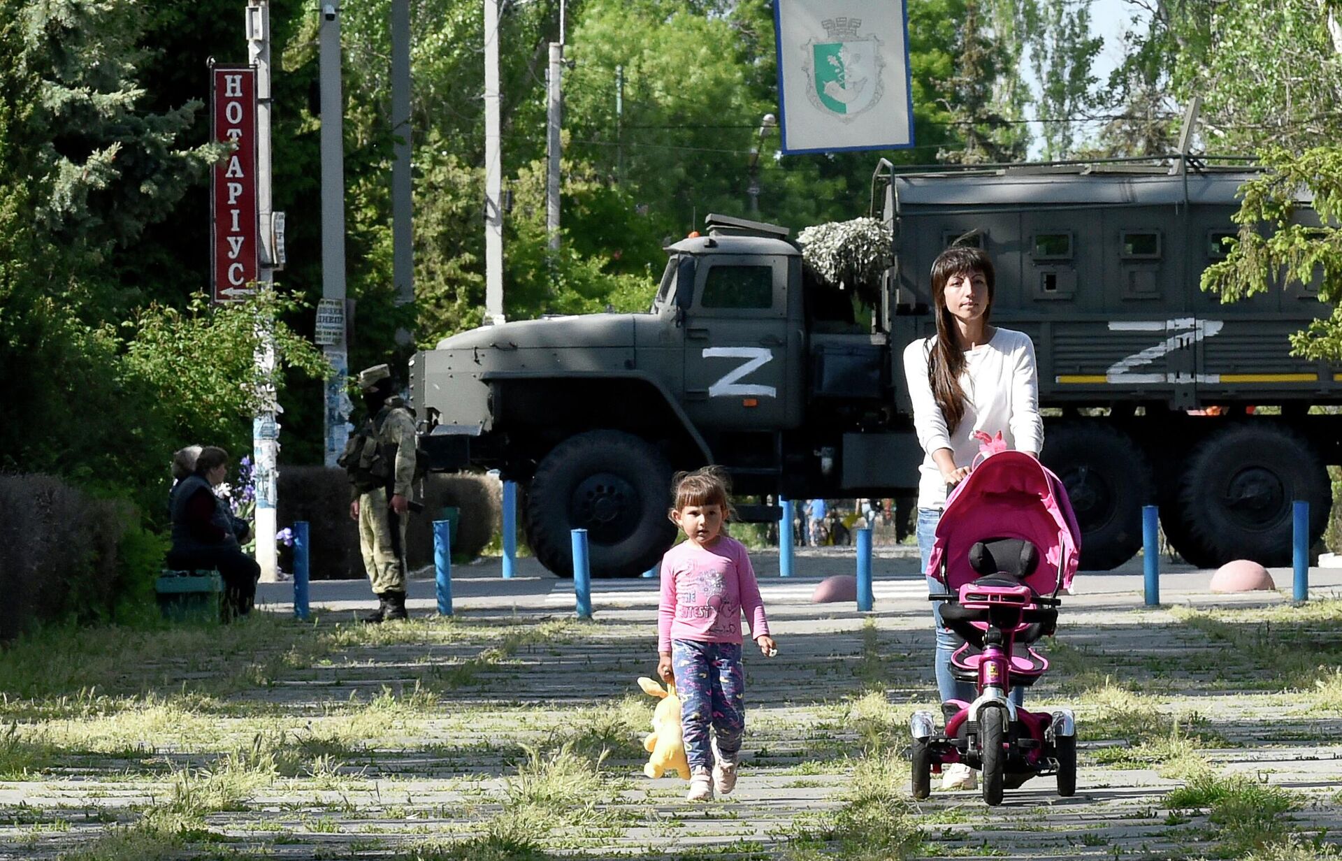 This photo taken on May 20, 2022 shows a womand and child walking in a park as Russian servicemen patrol  the street in Skadovsk, Kherson Oblast, amid the ongoing Russian military action in Ukraine - Sputnik International, 1920, 20.09.2022
