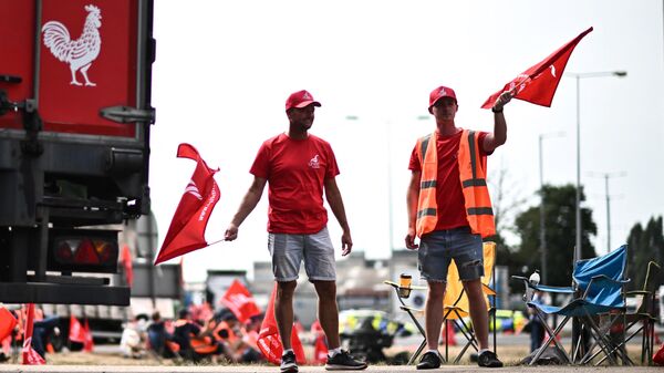 Dock workers wave flags of the trade union Unite the Union as they take part in a demonstration at a picket line outside the entrance of the UK's largest freight port, in Felixstowe, on August 22, 2022, during a eight-day strike over pay - Sputnik International