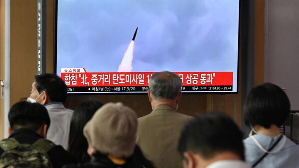 People watch a television screen showing a news broadcast with file footage of a North Korean missile test, at a railway station in Seoul on October 4, 2022 - Sputnik International