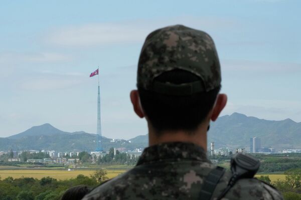 A North Korean flag flutters in the wind as a South Korean army soldier stands guard at the border villages of Panmunjom in Paju, South Korea, Tuesday, Oct. 4, 2022. - Sputnik International