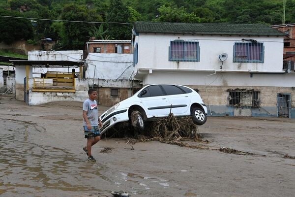 A resident walks past a car washed away by a landslide during heavy rains in Las Tejerias, Aragua state, Venezuela, on October 9, 2022. - Sputnik International