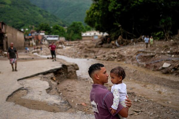 A man holds his daughter next to an overflow revine that triggered flooding in Las Tejerias, Venezuela, Sunday, Oct. 9, 2022. - Sputnik International