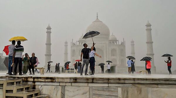 Tourists hold umbrellas and pose for pictures as they visit the Taj Mahal during a downpour in Agra on October 9, 2022. - Sputnik International