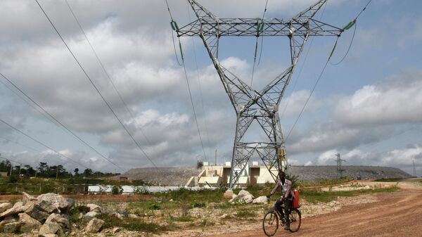 A man rides a bicycle under electrical power lines eminating from the electricity production plant of the Soubre hydroelectric dam on March 6, 2017 in Soubre. - The Soubre hydroelectric dam, built by China to reduce the energy deficit in the Ivory Coast, will be commissioned at the end of March, a project official said March 7.  - Sputnik International