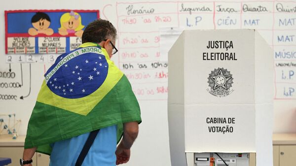 A man with a Brazilian national flag on his shoulders votes at a polling station in Brasilia, on October 30, 2022, during the presidential run-off election. - Sputnik International