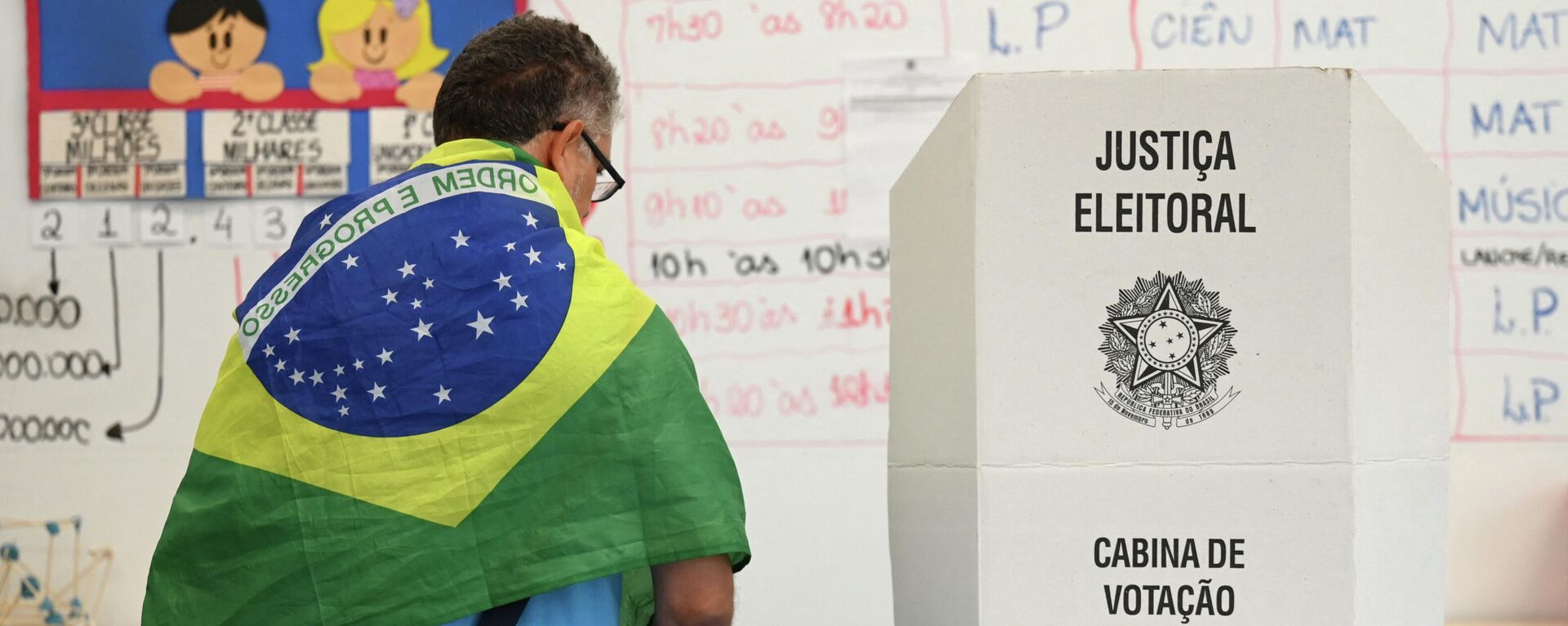 A man with a Brazilian national flag on his shoulders votes at a polling station in Brasilia, on October 30, 2022, during the presidential run-off election. - Sputnik International, 1920, 22.11.2022