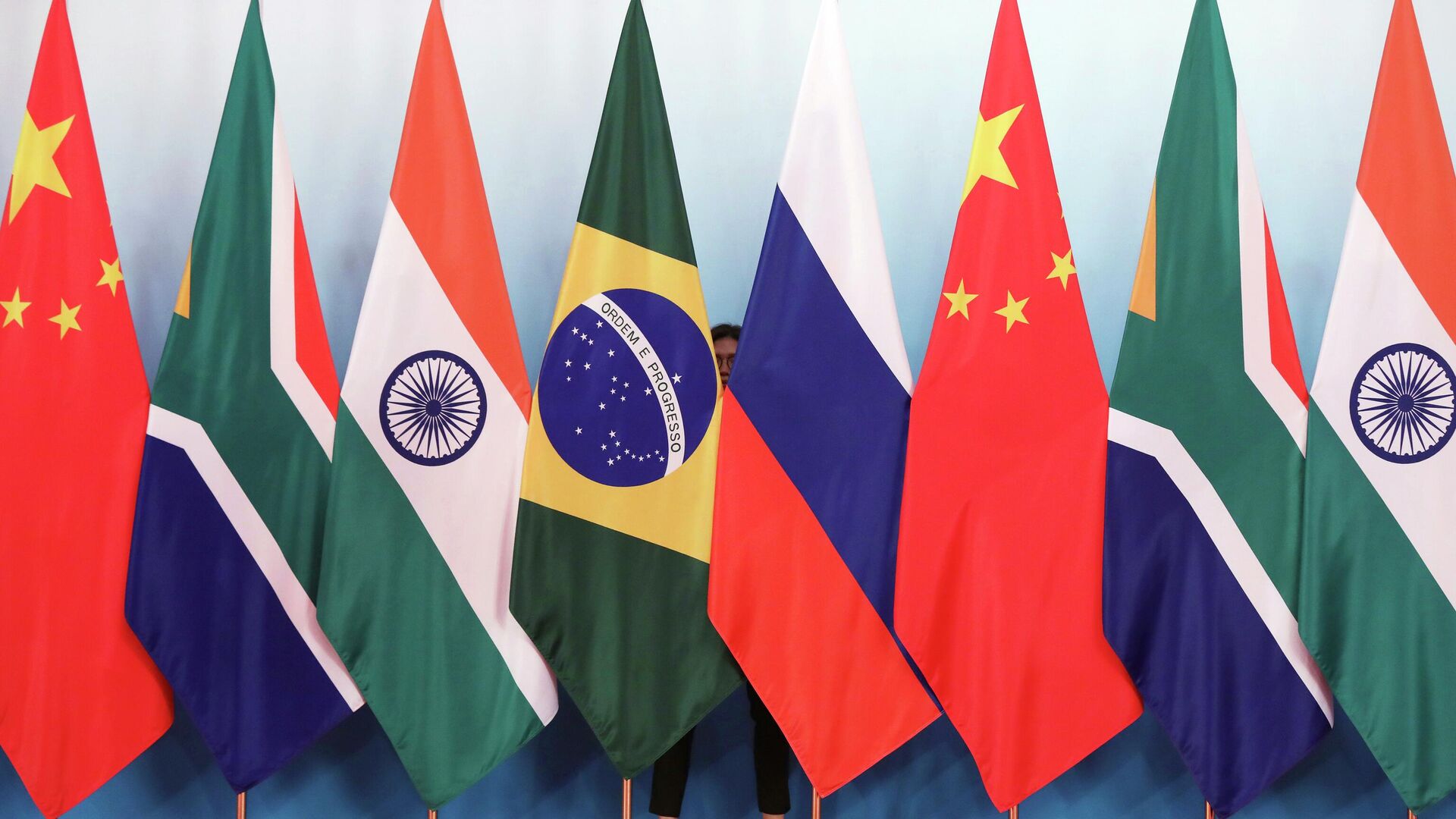 Staff worker stands behind national flags of Brazil, Russia, China, South Africa and India to tidy the flags ahead of a group photo during the BRICS Summit at the Xiamen International Conference and Exhibition Center in Xiamen, southeastern China's Fujian Province, Monday, Sept. 4, 2017. - Sputnik International, 1920, 28.11.2022