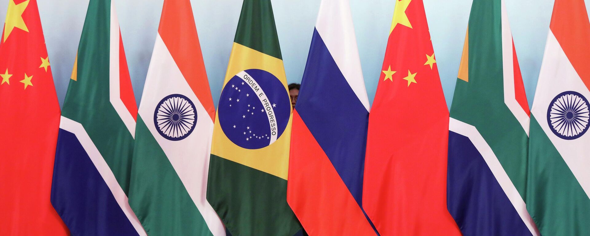 Staff worker stands behind national flags of Brazil, Russia, China, South Africa and India to tidy the flags ahead of a group photo during the BRICS Summit at the Xiamen International Conference and Exhibition Center in Xiamen, southeastern China's Fujian Province, Monday, Sept. 4, 2017. - Sputnik International, 1920, 06.04.2023