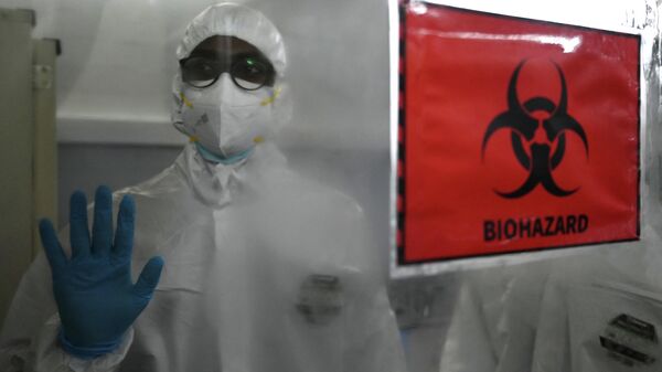 A technician wearing personal protective equipment (PPE) gestures next to  a biohazard sign inside a molecular laboratory facility set up to test for the monkeypox disease. - Sputnik International
