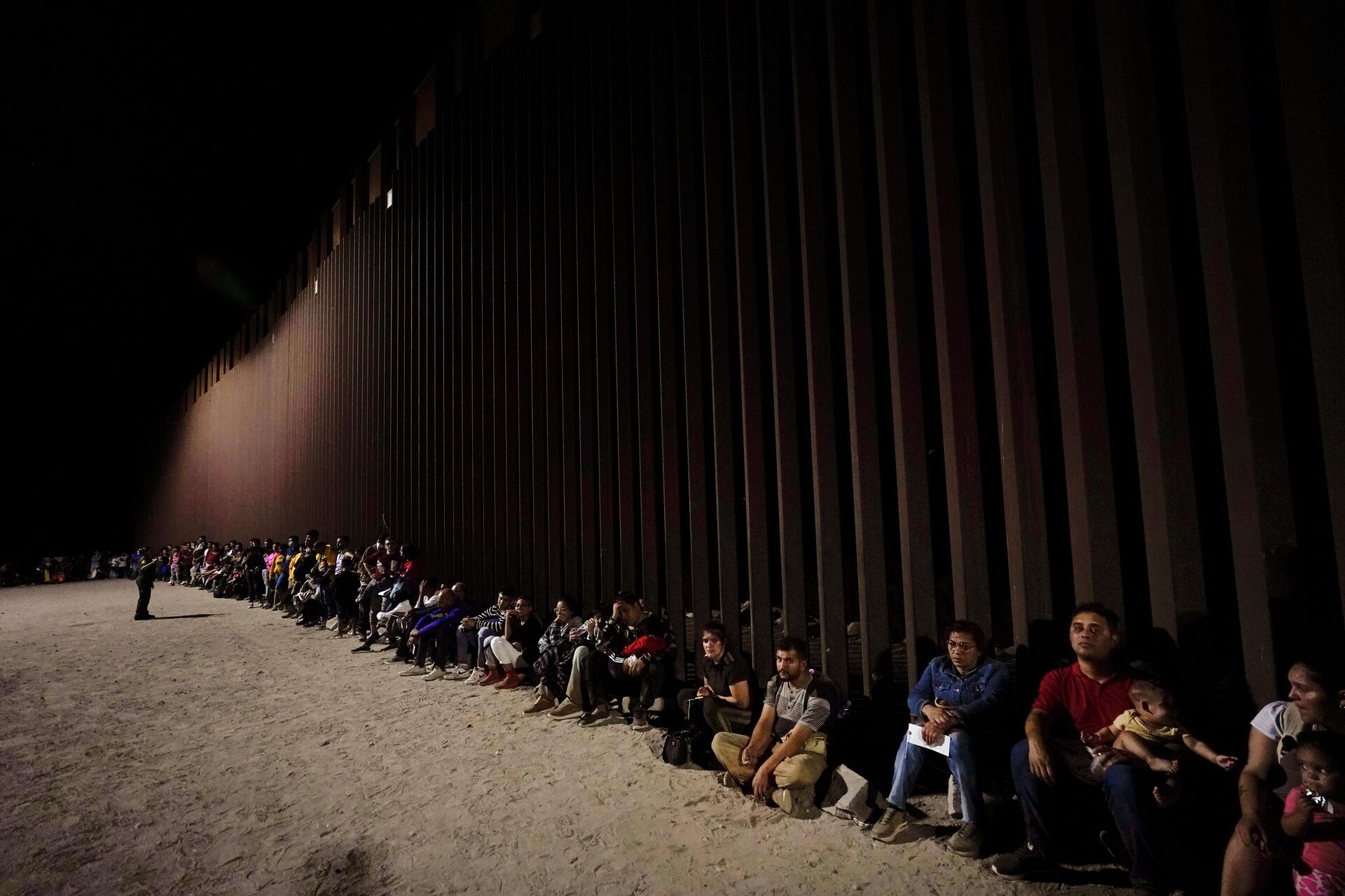 Migrants wait along a border wall Aug. 23, 2022, after crossing from Mexico near Yuma, Ariz. - Sputnik International, 1920, 10.01.2023