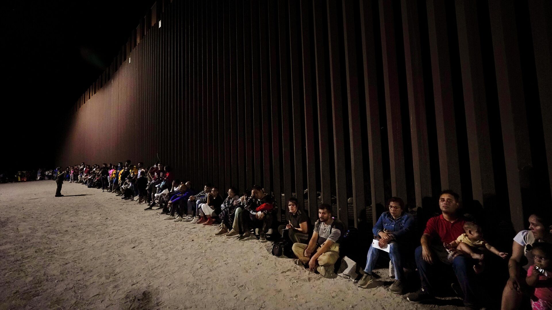 Migrants wait along a border wall Aug. 23, 2022, after crossing from Mexico near Yuma, Ariz. - Sputnik International, 1920, 27.12.2022
