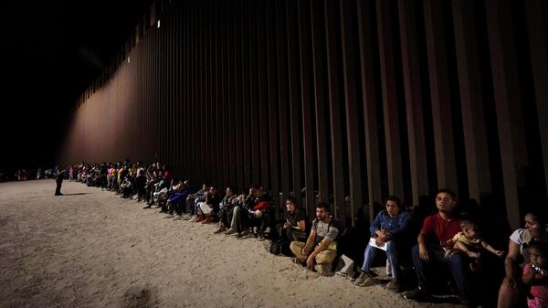 Migrants wait along a border wall Aug. 23, 2022, after crossing from Mexico near Yuma, Ariz. - Sputnik International