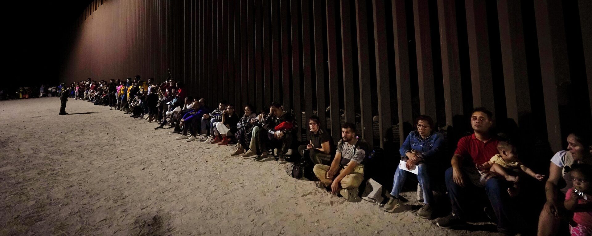 Migrants wait along a border wall Aug. 23, 2022, after crossing from Mexico near Yuma, Ariz. - Sputnik International, 1920, 28.10.2023