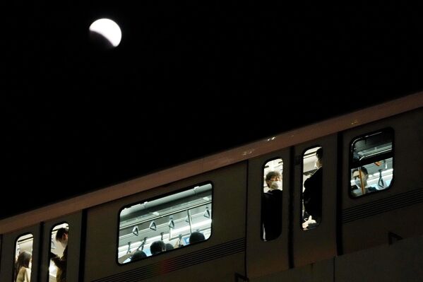Люди едут в поезде во время лунного затмения, наблюдаемого в Токио - Sputnik International