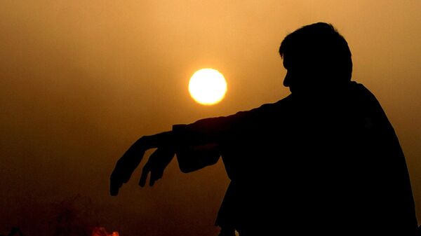 A Pakistani man warms himself beside a fire during last sunset of the year 2006 on a hill above Karachi, 31 December 2006 - Sputnik International