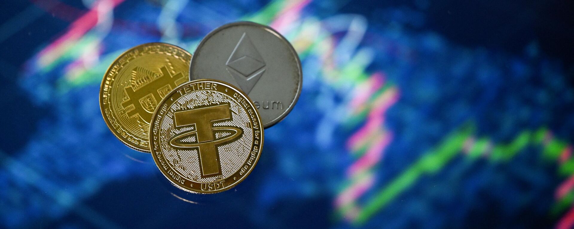 An illustration picture taken in London on May 8, 2022, shows gold plated souvenir cryptocurrency Tether (USDT), Bitcoin and Etherium coins arranged beside a screen displaying a trading chart. - Sputnik International, 1920, 13.12.2022