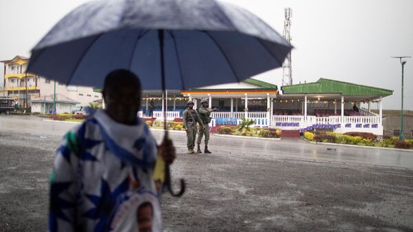 A supporter of the ruling CPDM party, Cameroon People's Democratic Movement of incumbent Cameroonian President Paul Biya, uses an umbrella to protect from the rain as a patrol of the Cameroonian Gendarmerie deploys in the Omar Bongo Square Square of the majority anglophone South West province capital Buea, on October 3, 2018 on the sidelins of a political rally. - Sputnik International