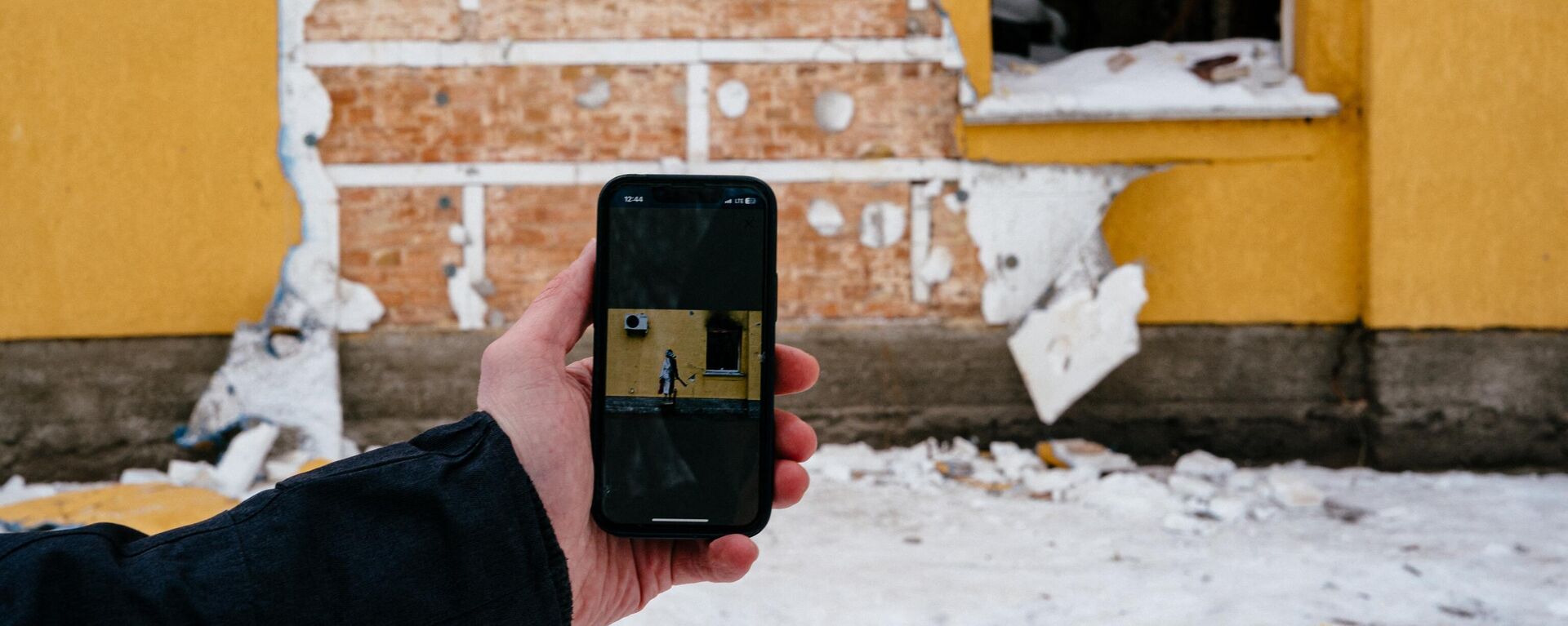 This photograph taken on December 3, 2022 shows a mobile phone with Banksy's work on the screen in front of a cut off of the wall of a damaged building from where a group of people tried to steal this work of the famous British artist in the town of Gostomel, near Kiev. - Sputnik International, 1920, 03.12.2022