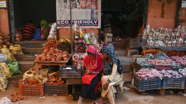 In this photograph taken on October 4, 2019, women use a mobile phone as they sit outside their shop displaying items made of clay, at Kumhar Gram (Potter's Village) in New Delhi. - Sputnik International